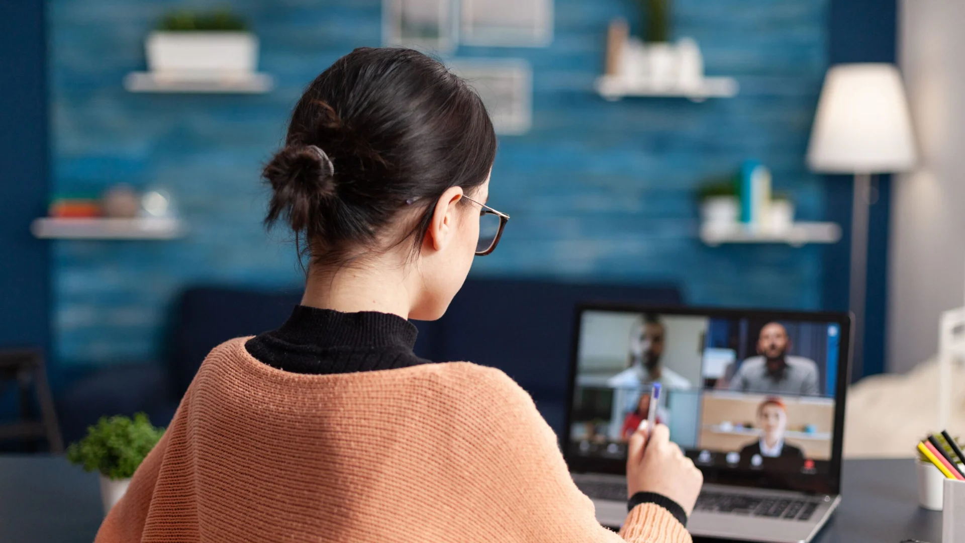 Rückansicht einer Frau am Schreibtisch, die an einem Video-Webinar mit vier Teilnehmern zum Thema Pflege teilnimmt.