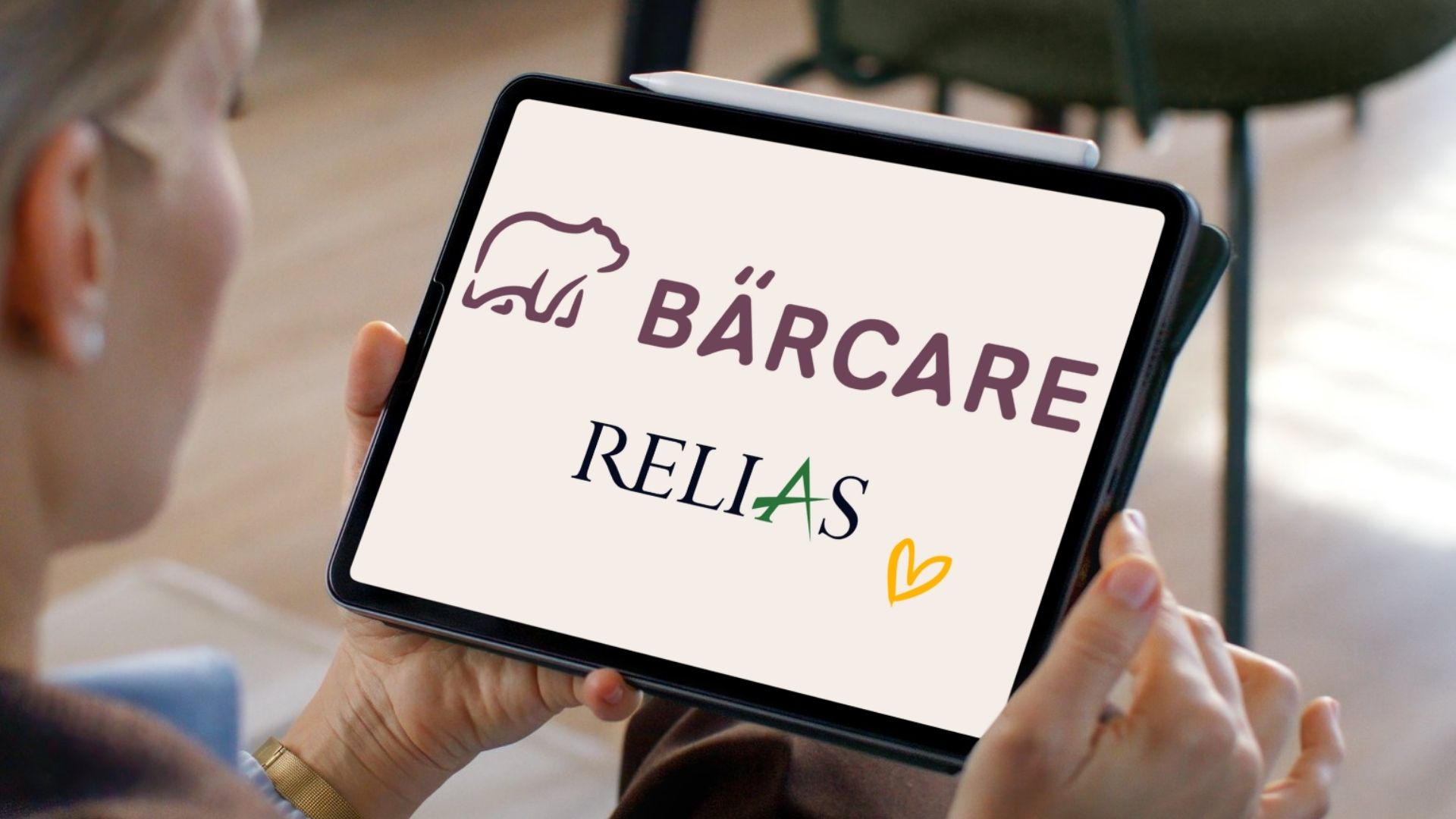 Eine Person hält ein Tablet, auf dem die Logos von Bärcare und Relias sowie ein gelbes Herz die Partnerschaft symbolisieren.